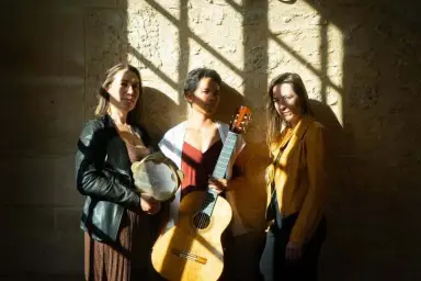 Le Trio Kalakou : trois musiciennes avec percussions, guitare et chant, devant un mur de pierre.