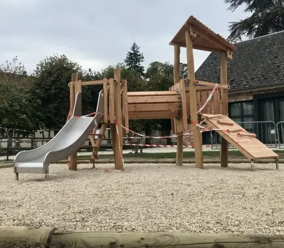 La nouvelle aire de jeux terminée sur la place du village : structure de jeu en bois avec toboggan métallique, devant l'école.