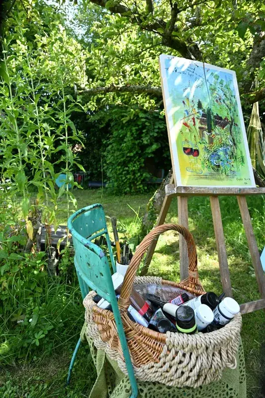Chevalet et panier de matériel de peintre installés dans un jardin verdoyant.