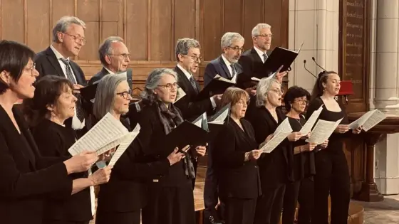 Chorale en tenue noire, partitions en main, chantant dans l'église de Saint-Denis-le-Ferment devant les boiseries.