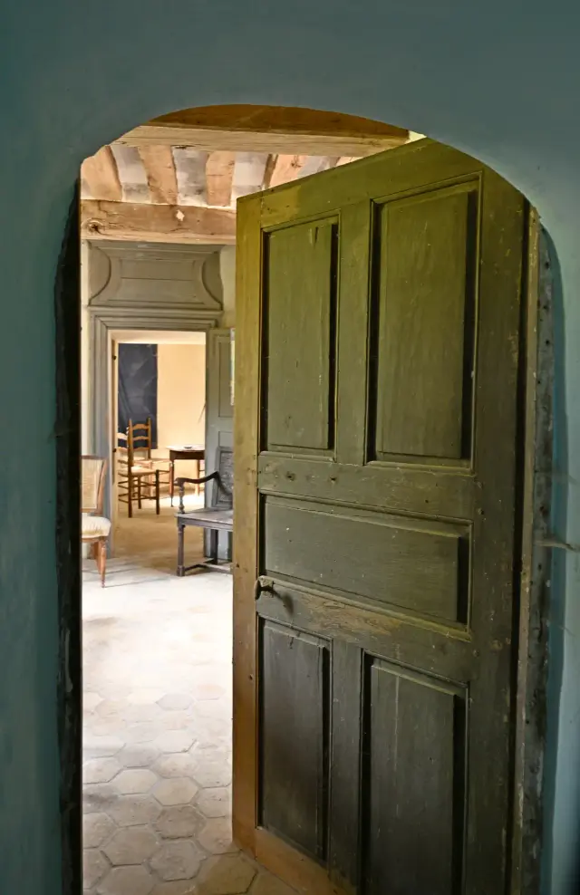 Porte ancienne ouverte sur une pièce aux tomettes et poutres